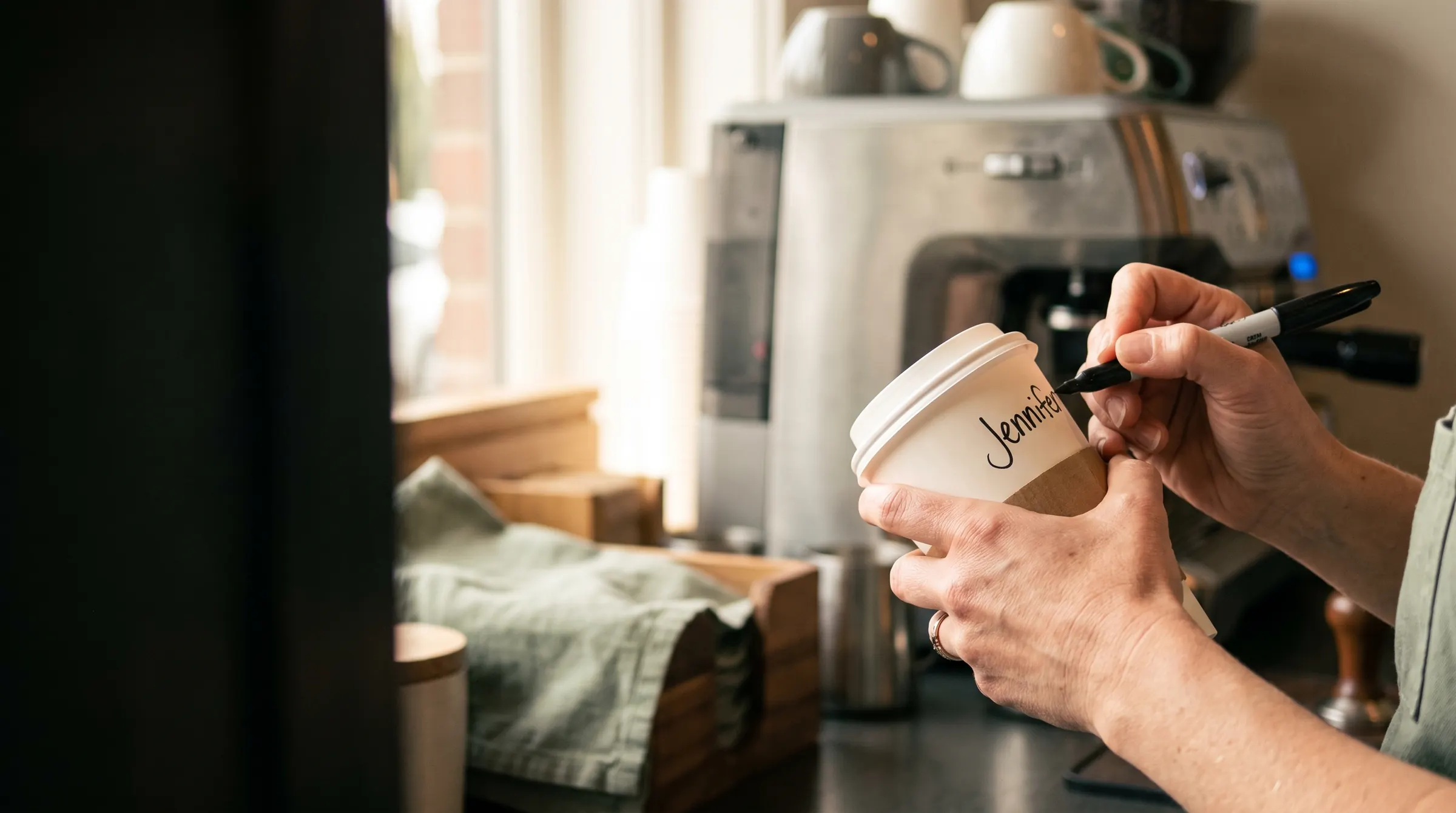 A barista writes “Jennifer” on a coffee cup